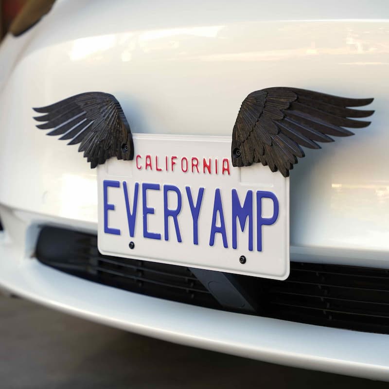 A California license plate reading EVERYAMP is attached to a white car, with decorative black wings extending from each side of the plate.