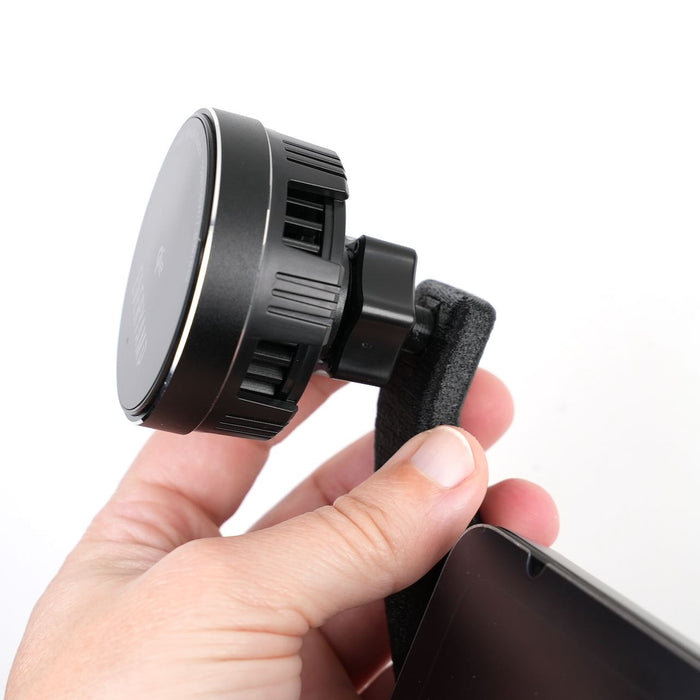 A person holds a black, circular magnetic phone holder with one hand, attaching it to a fabric-covered car vent mount.