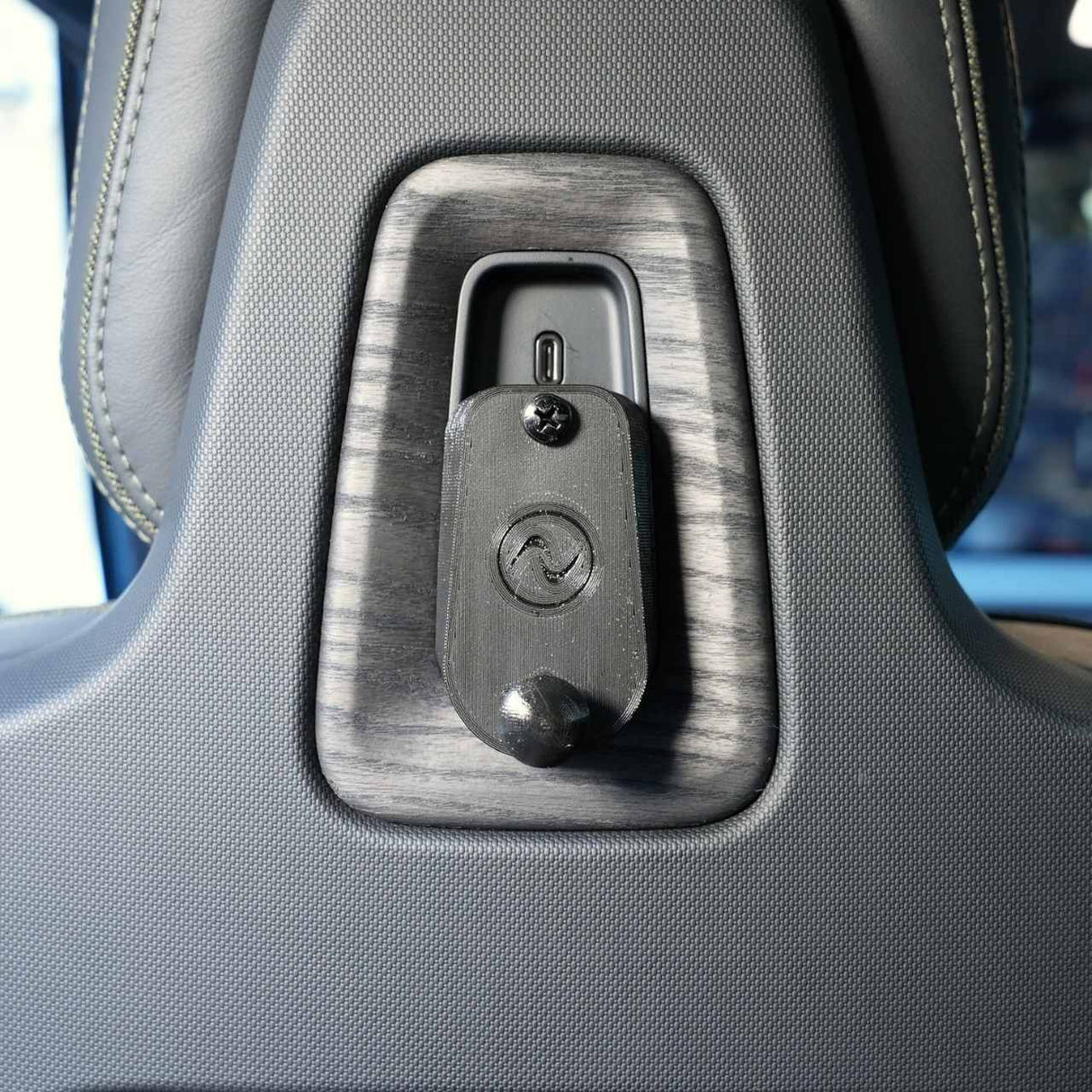 Close-up of the EveryAmp Back Seat Tablet/Phone Mount Anchor for Rivian R1T and R1S on a car seat headrest, featuring textured upholstery, wood trim, and a 3D-printed mount—perfect for organized travel.