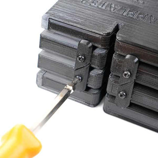 A screwdriver with an orange handle tightening a screw on a black 3D-printed object with a textured surface.