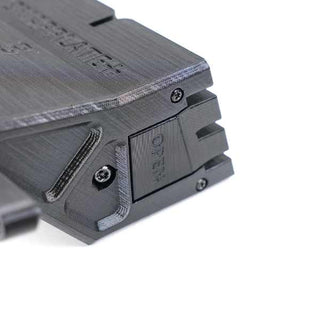Close-up of a 3D-printed plastic object with visible screws and an OPEN label on one side. The object appears to have a mechanical function or part of a larger assembly.