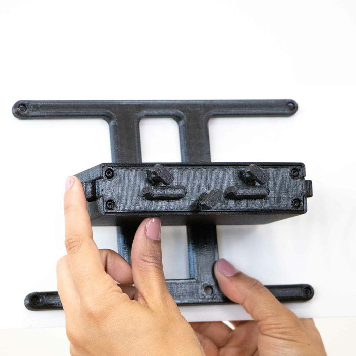 Hands holding a black plastic mount with adjustable knobs and a T-shaped bracket.