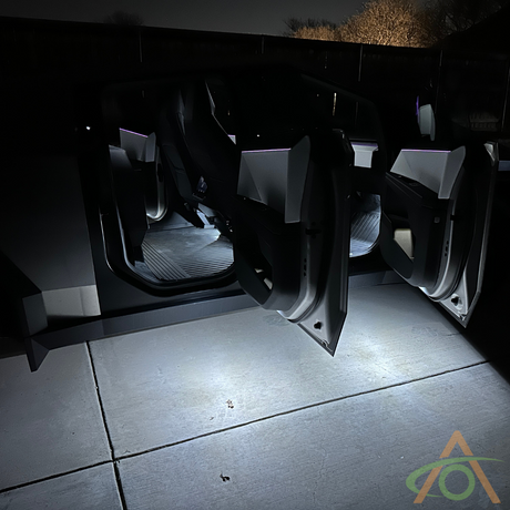 The Cybertruck, fitted with Abstract Oceans white Ultrabright Lights, stands illuminated against a nighttime backdrop with its gull-wing doors open.