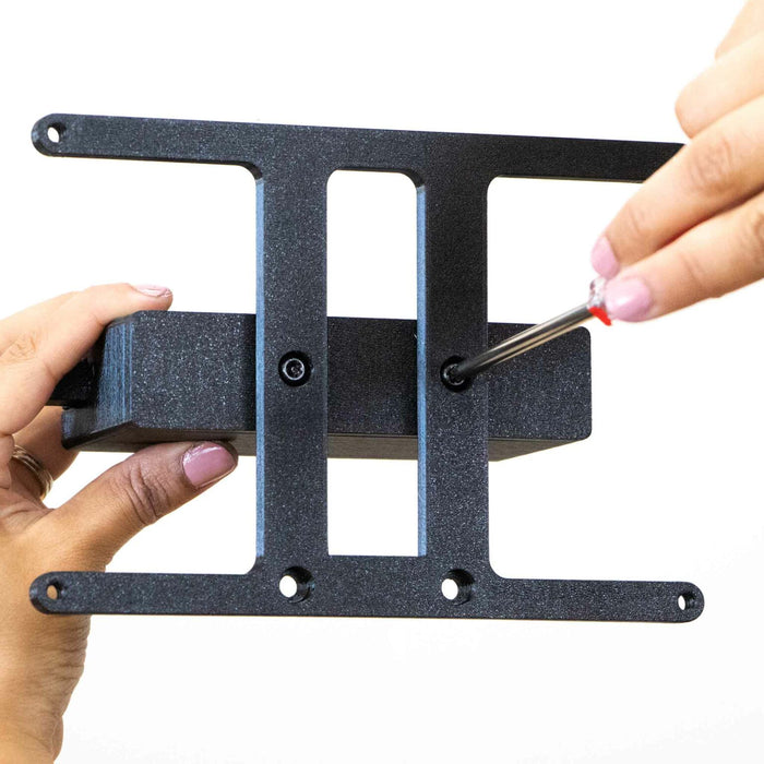 Hands using a screwdriver to secure a black metal bracket.