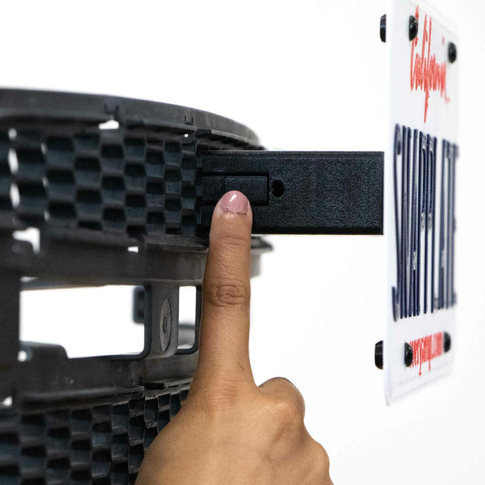 A hand with a pink nail pushes a button next to a California license plate attached to a black textured surface.