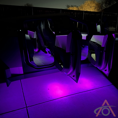 A Cybertruck with open doors and Abstract Oceans Ultrabright Purple Lights casts a vibrant glow on the driveway at night.