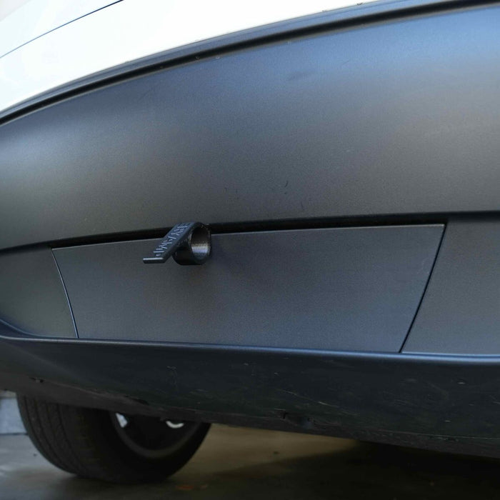 A close-up of a cars rear bumper with a trailer hitch cover. The cover is black and attached securely to the bumper.