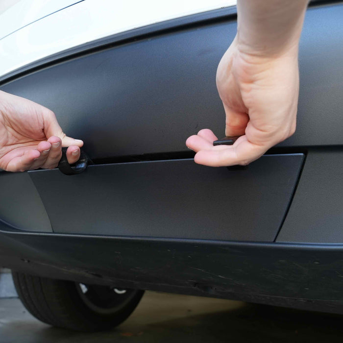 Hands attaching a cable to the rear underside of a car.