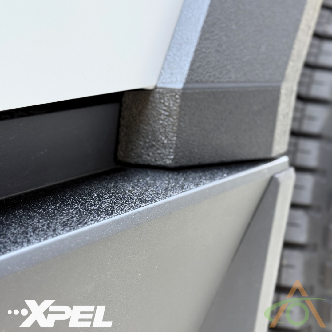 Close-up image of a textured black surface with a grey panel, prominently featuring the XPEL logo in the corner, showcasing Abstract Oceans Ultra-Tough Xpel Armor Rear Bumper Protection for Cybertruck.