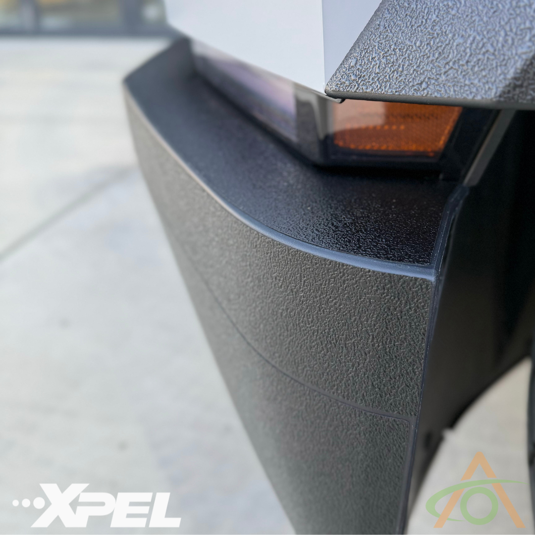 Close-up of a Cybertrucks textured bumper with sharp edge and orange reflector featuring Ultra-Tough Xpel Armor by Abstract Ocean, highlighting the advanced protection film that seamlessly complements the trim.