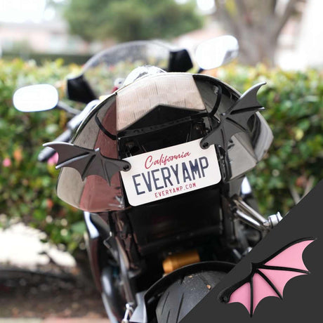 A black motorcycle with California SnapPlates, displaying the EveryAmp plate, EVERYAMP, has License Plate Bat Wings attached at the rear. Blurred trees and foliage in the background suggest a fast-paced journey.