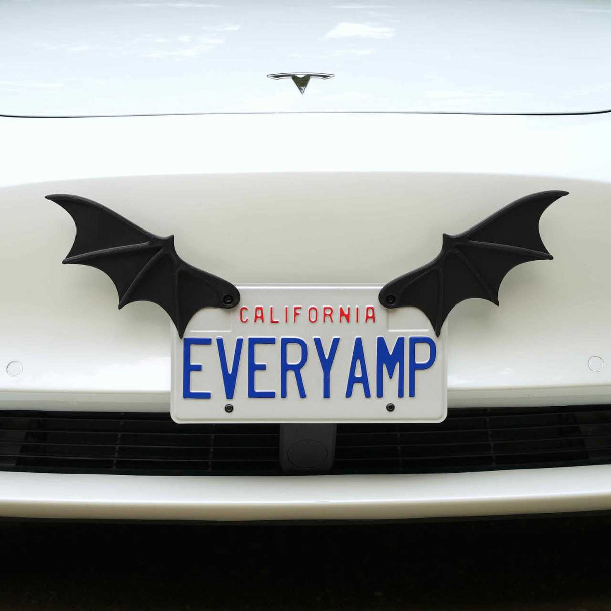 A white Tesla with California plates reading EVERYAMP displays black License Plate Bat Wings by EveryAmp, mounted on a SnapPlate made from recycled PETG plastic.