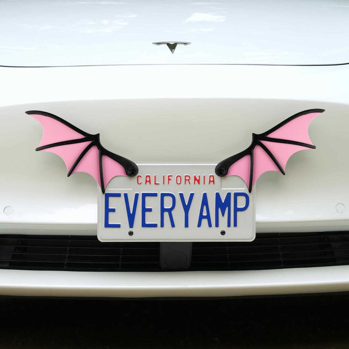 A white car displays a front SnapPlate featuring EveryAmp, adorned with License Plate Bat Wings in pink, made from recycled PETG plastic on each side.