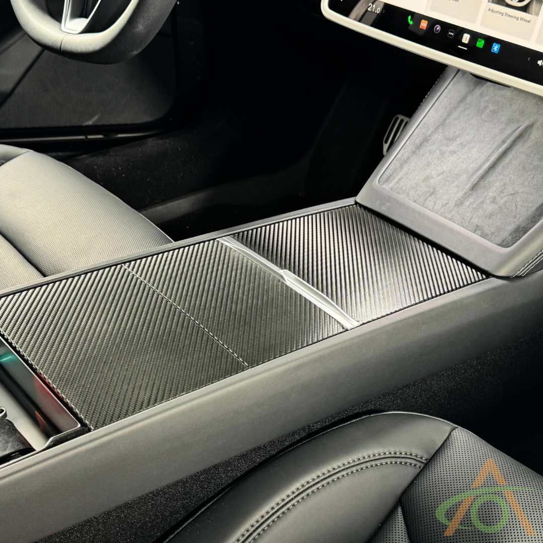 Close-up of a Tesla center console featuring the Abstract Ocean Center Console Vinyl Wrap for Refreshed Model 3 & Y, with a carbon fiber-style finish, touchscreen display, and front seats—ideal for adding style with premium 3M 2080 vinyl.