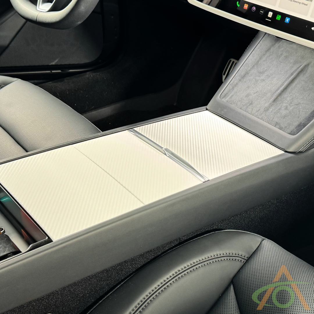 Interior view of a car highlighting the Abstract Ocean Center Console Vinyl Wrap for Refreshed Model 3 & Y on the sliding center console cover, along with the front passenger seat and part of the touchscreen dashboard.