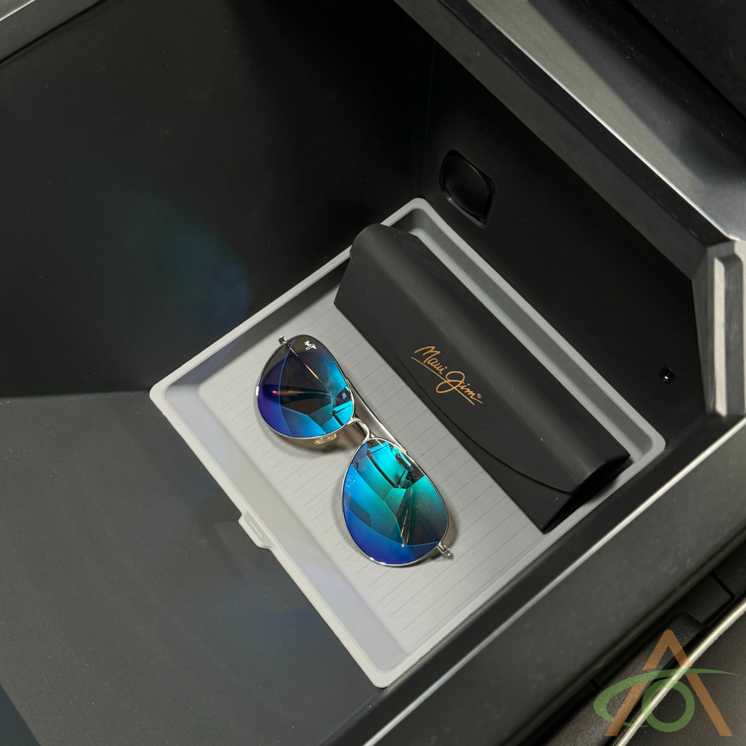A pair of sunglasses with blue reflective lenses rests in a sleek black Maui Jim case, nestled comfortably within the Abstract Ocean Center Console Liner for Cybertruck among essentials.