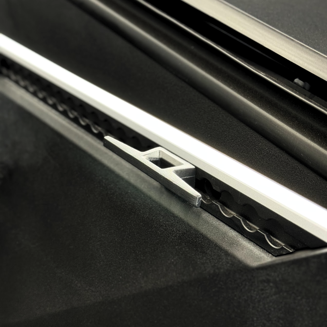 Close-up of a Cybertruck L-Track Accessories paper cutter by Abstract Ocean, featuring a silver aluminum alloy handle and serrated cutting edge. The partially open cutter reveals its OEM-quality black internal mechanism.