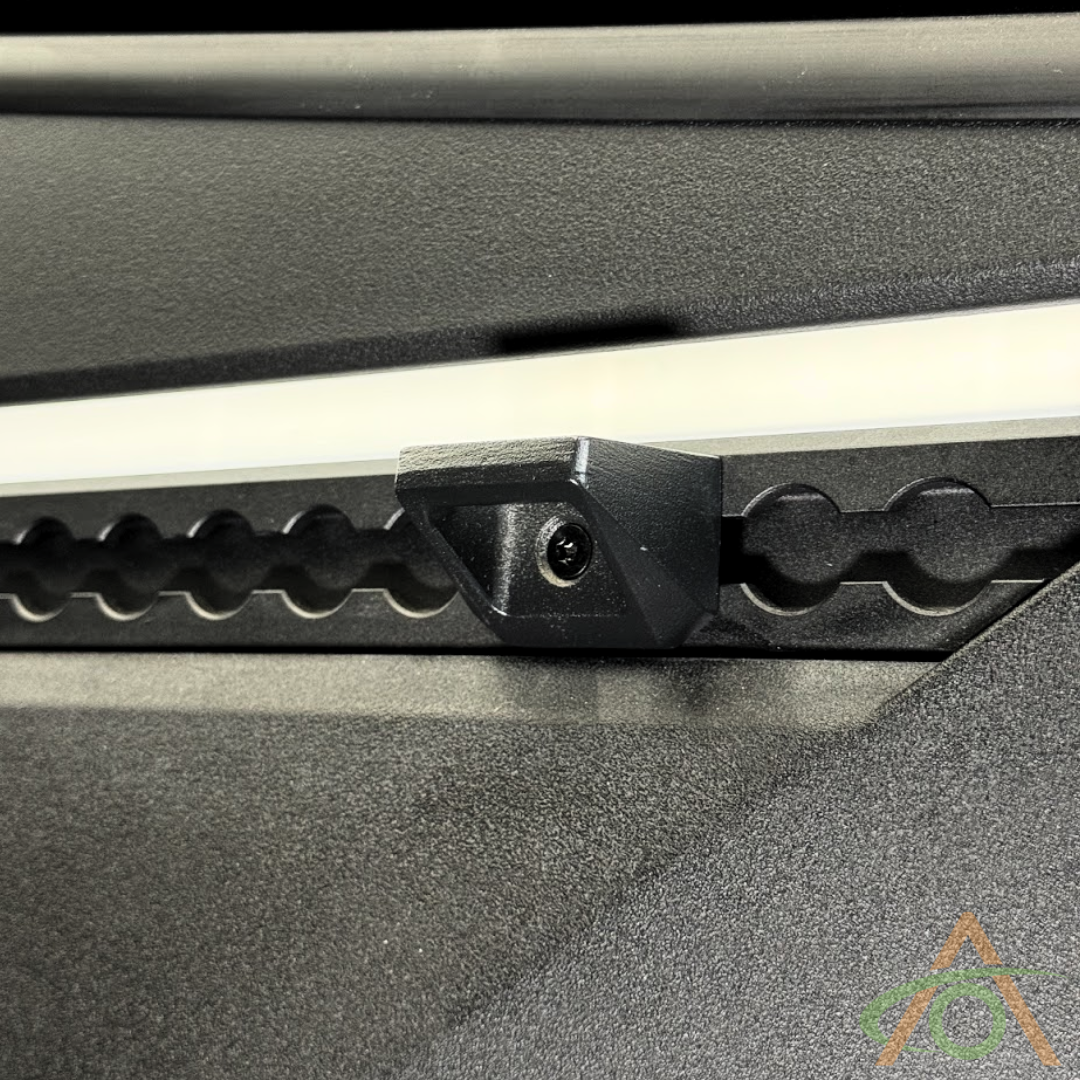 A close-up of the Abstract Ocean Cybertruck L-Track Accessory, a triangular black metal bracket made from cast aluminum alloy. Attached to a textured surface with a gear-tooth pattern, it is securely fastened by a small screw, demonstrating OEM-quality craftsmanship.