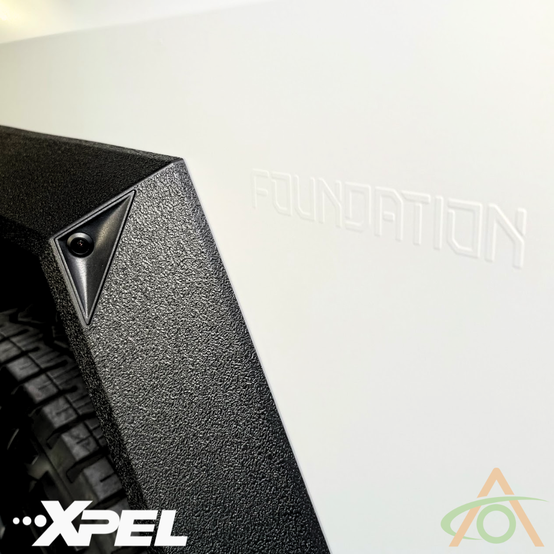 A textured black part with a camera is on a white surface embossed with FOUNDATION. Logos for XPEL and another company highlight Abstract Oceans Ultra-Tough Xpel Armor Fender Flares, showcasing its protective role for the Cybertrucks plastic trim.