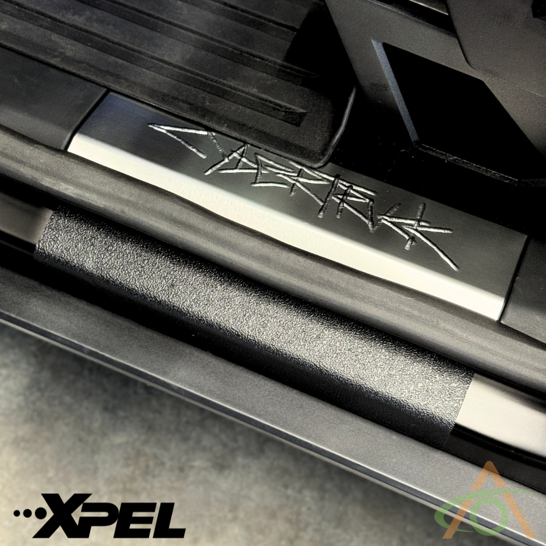 The close-up of the Cybertruck door sills reveals Cybertruck in metallic font, with black textured trim featuring Abstract Oceans Ultra-Tough Xpel Armor Protection, subtly showcasing the Xpel logo, emphasizing its premium quality.