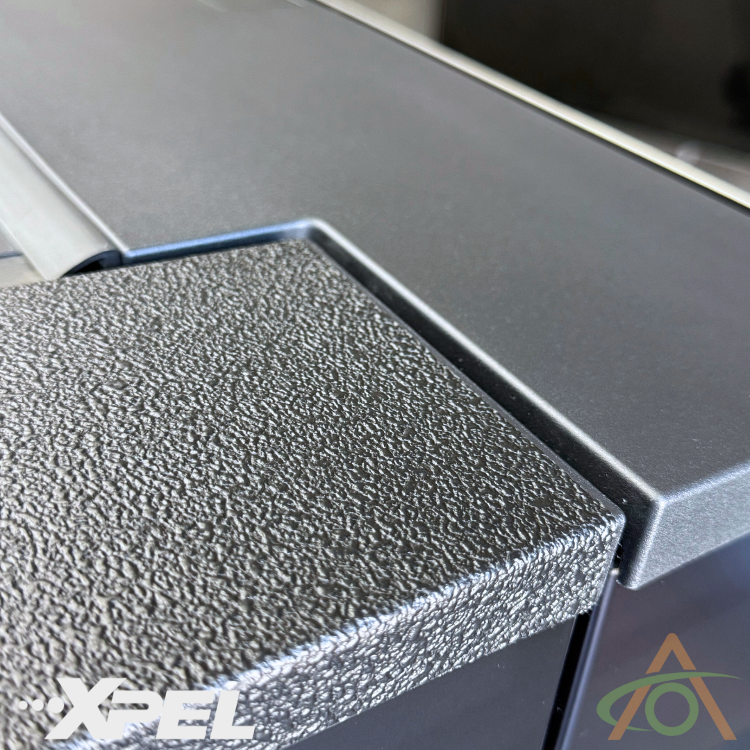 A textured black corner close-up features the Abstract Ocean logo next to an emblem, recalling Cybertruck protection with Ultra-Tough Xpel Armor Bed Protection.