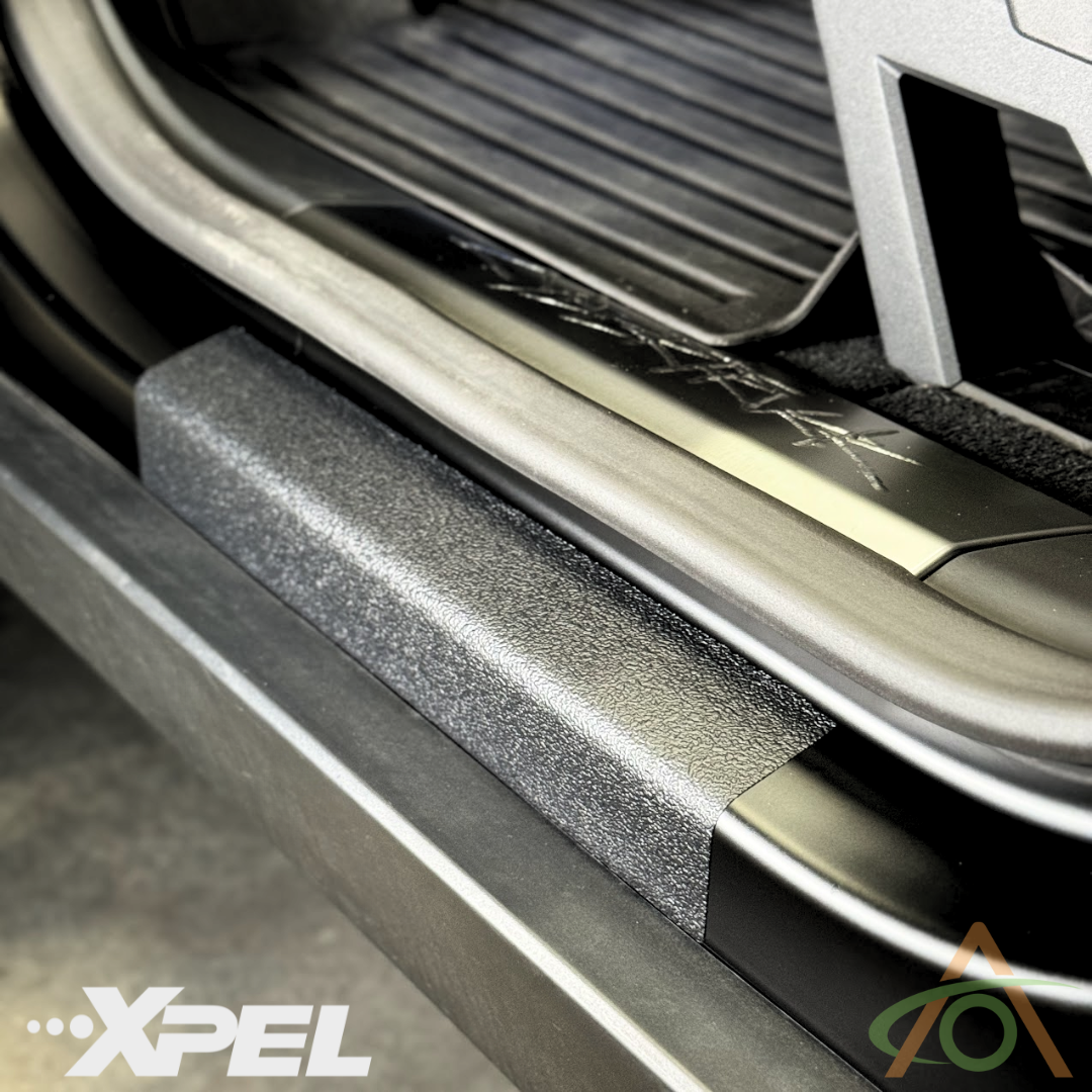 Close-up of a Cybertruck door sill, shielded by Abstract Oceans Ultra-Tough Xpel Armor Door Sill Protection, featuring a branded logo in the corner to highlight the durability of this textured defense.