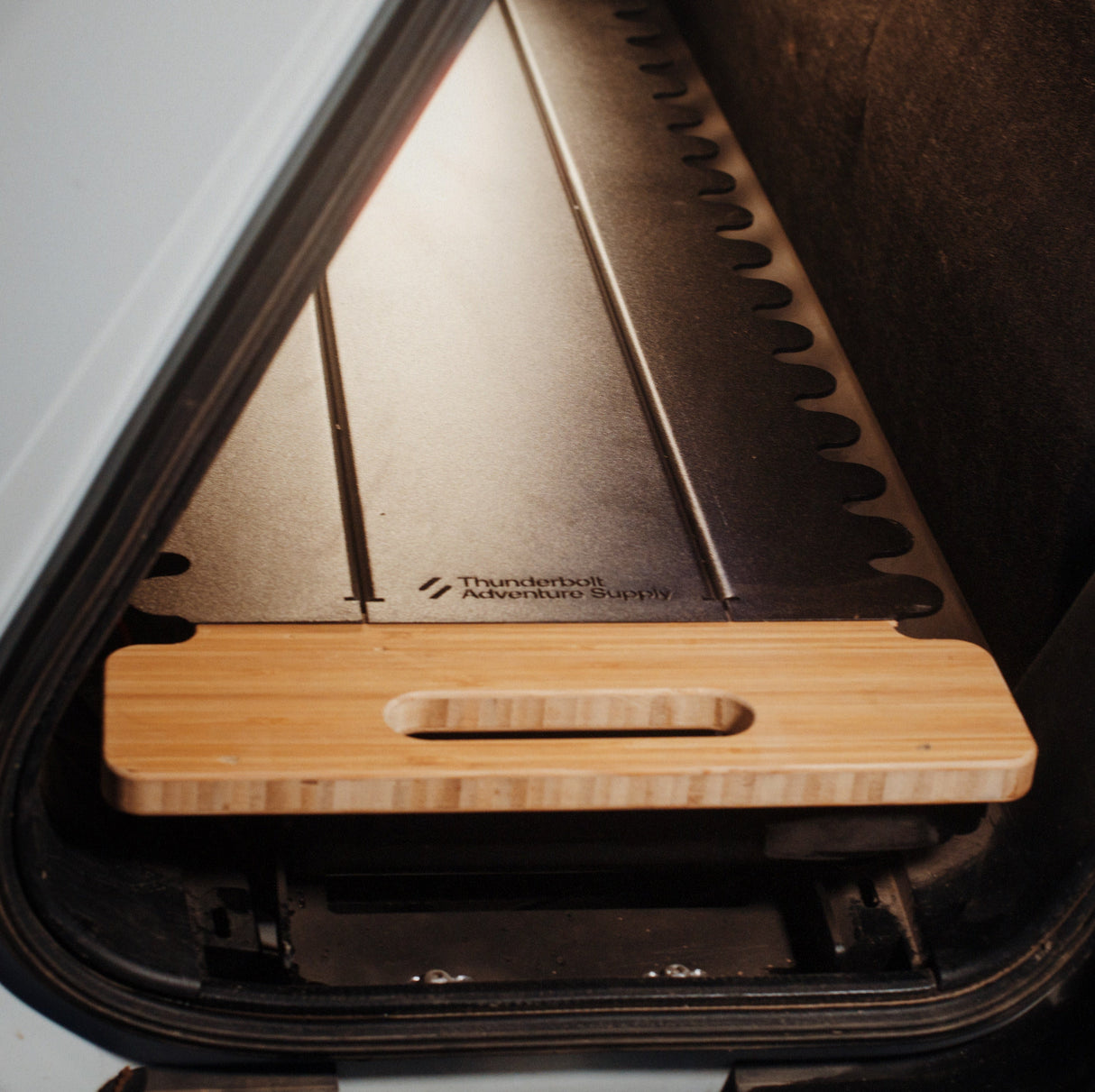 A wooden board with a handle slot, part of the Thunderbolt Adventure Supply Rivian R1T - Overland Kitchen with updated Gear Sled, is partially pulled out from a customized storage compartment.