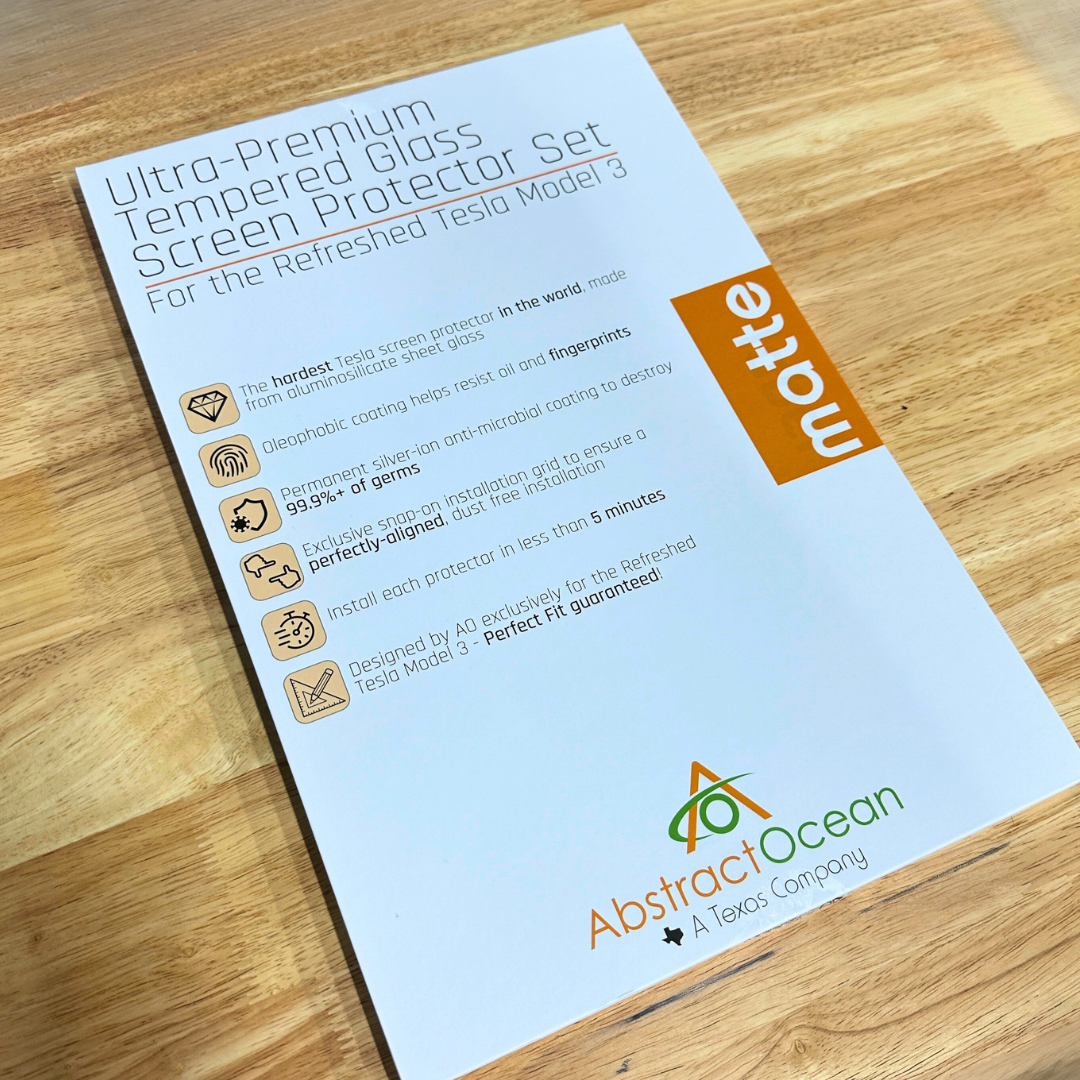 A product sheet on a wooden surface displays Abstract Ocean's Ultra-Premium Tempered Glass (9H) Screen Protectors for the refreshed Model 3 & Y, featuring an advanced antimicrobial coating.