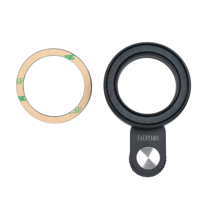 A black camera lens attachment with a small grip and a separate adhesive ring on a plain background.