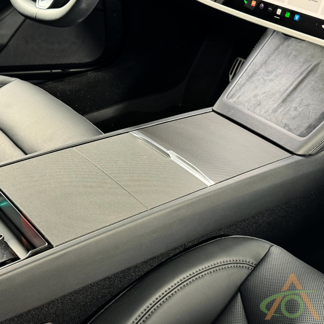 The image displays the Center Console Vinyl Wrap for Refreshed Model 3 & Y by Abstract Ocean, highlighting a sleek wrap on the center console with sliding cover and cup holders, set among black and gray seats.