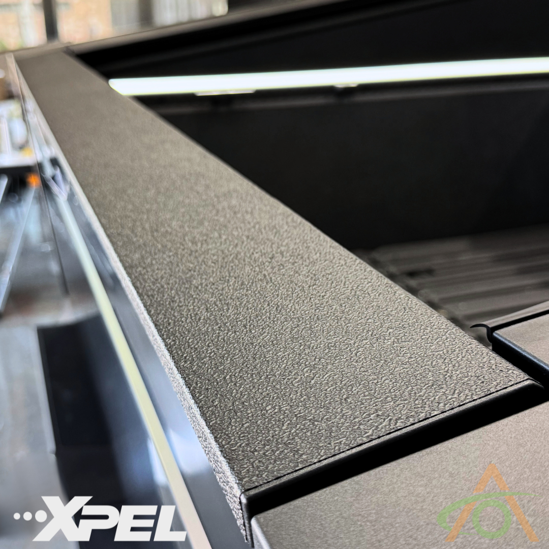 Close-up of the Ultra-Tough Xpel Armor Bed Protection by Abstract Ocean, showcasing the textured black finish and embossed logo for robust Cybertruck protection.
