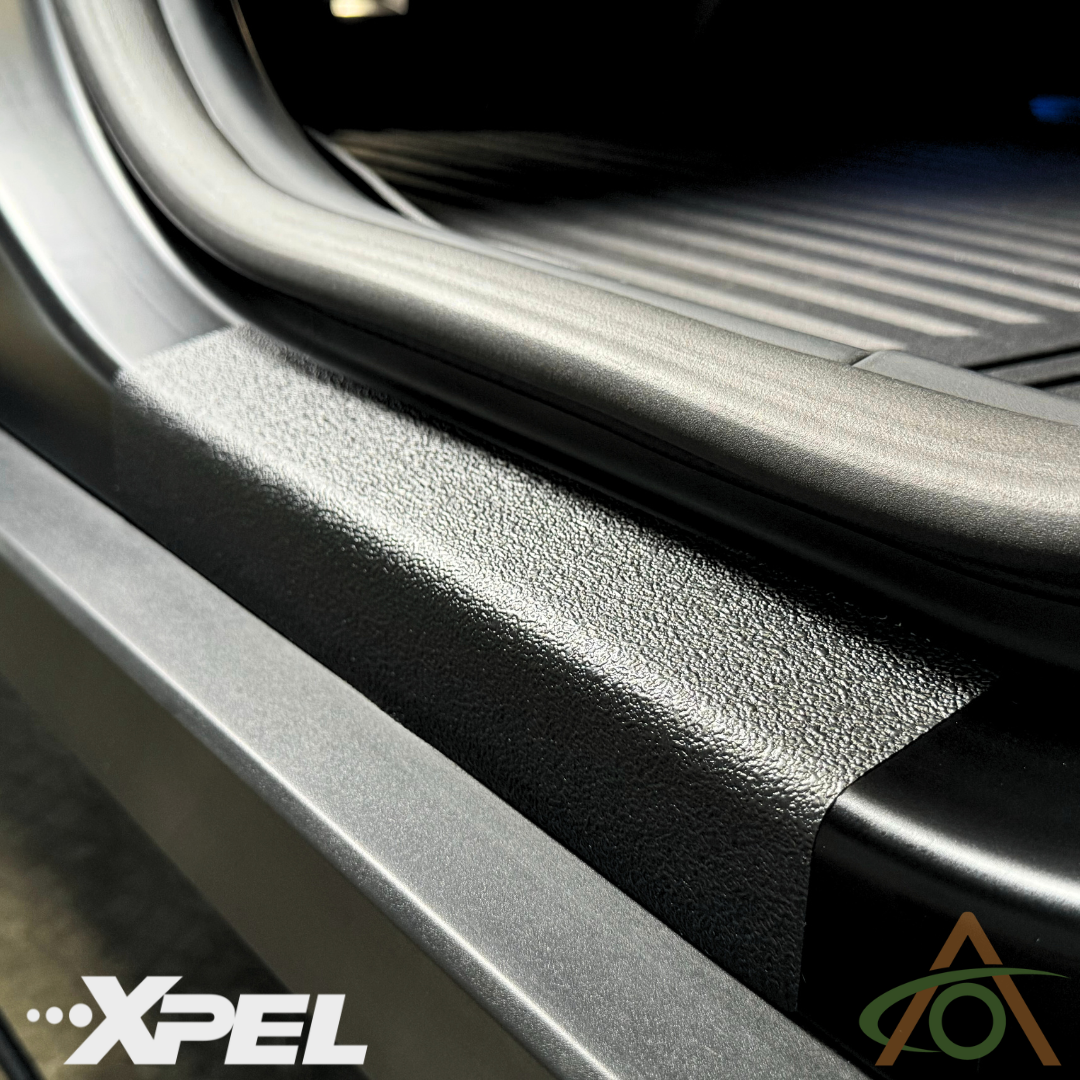 Close-up of Cybertruck door sills featuring Abstract Ocean’s Ultra-Tough Xpel Armor Protection film, displaying its textured surface for superior durability with visible logos in the corners.