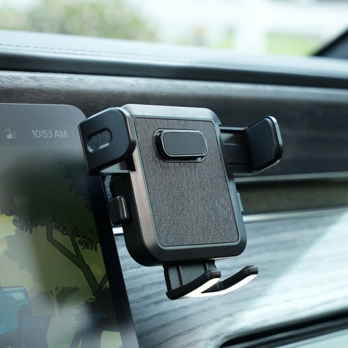 The EveryAmp Phone Mount Dash Anchor for Rivian R1T and R1S attaches to the car dashboard with adjustable arms and a textured surface, while a MagSafe charger integrates seamlessly next to it, alongside a digital display showcasing a colorful illustration against the wood grain finish.