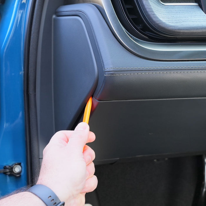 A person uses an orange plastic tool to pry open a panel on the interior door of a blue vehicle.