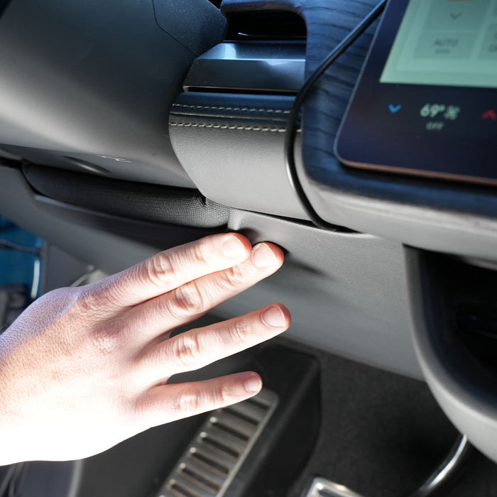 Hand pressing button near dashboard in a car interior, showing close-up of a display and air vent.