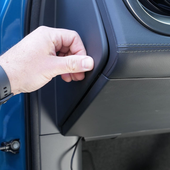 Hand pulling on the edge of a car’s dashboard cover, revealing a small gap.