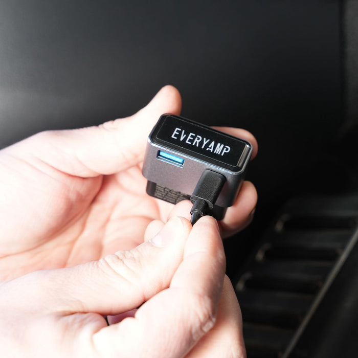 Hands holding a small electronic device labeled EVERYAMP with a USB port, as a cable is being plugged in.