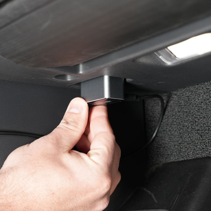 A hand plugging a small device into a port under a car dashboard.