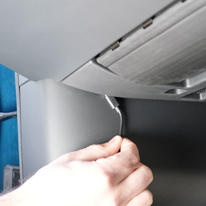 A hand plugs a cable into a port located beneath a dashboard inside a vehicle.