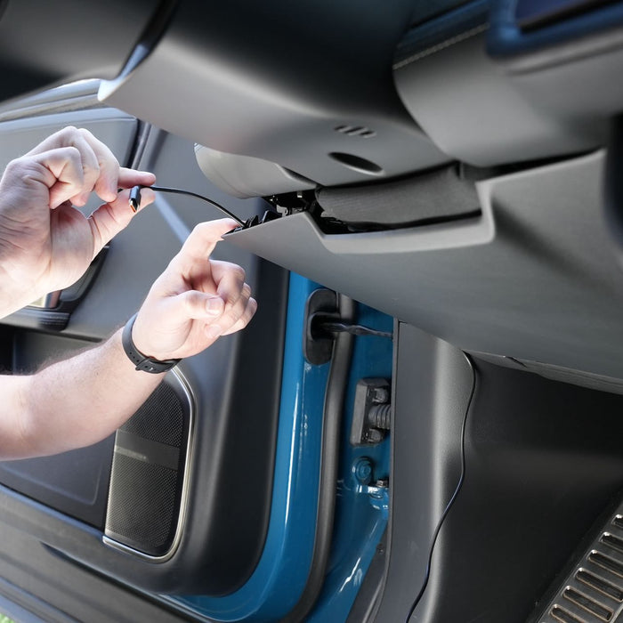 A person connects a cable to an open compartment under a car dashboard.