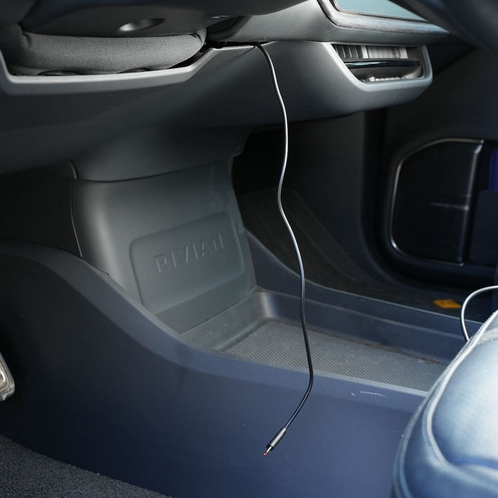 A single black cable hangs from the vehicle dashboard area, near the passenger seat and footwell. The cars interior is mostly grey with some blue trim visible.