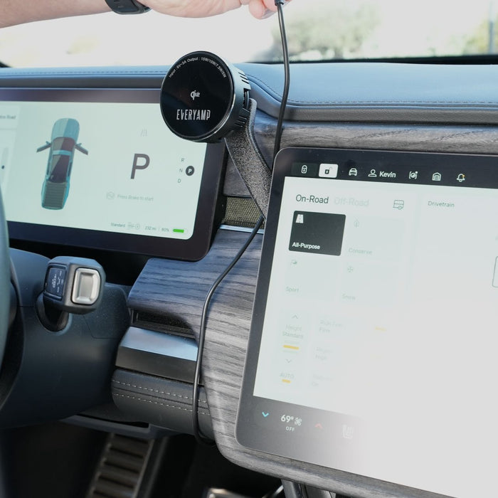 Person installing a circular device on an electric vehicles wooden dashboard. Two digital screens display vehicle information and settings.