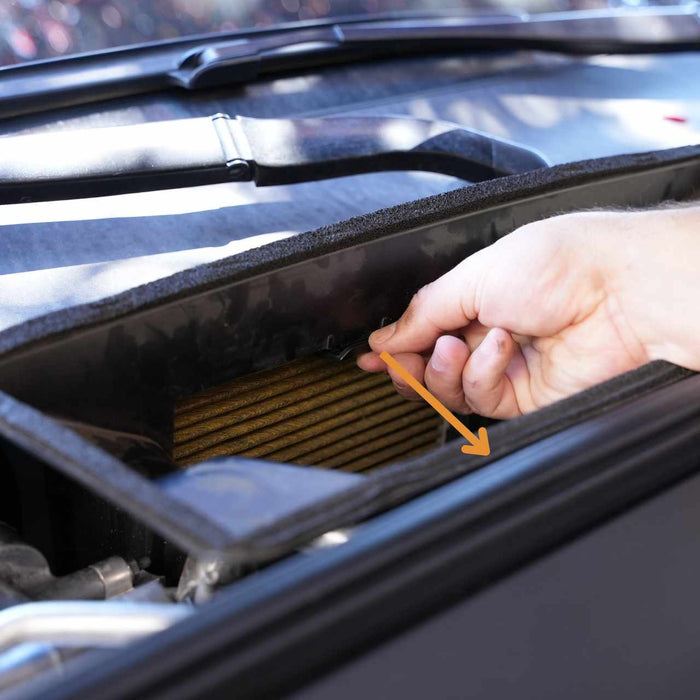 Hand pulling a car cabin air filter out of its compartment, with an arrow indicating the direction of removal.