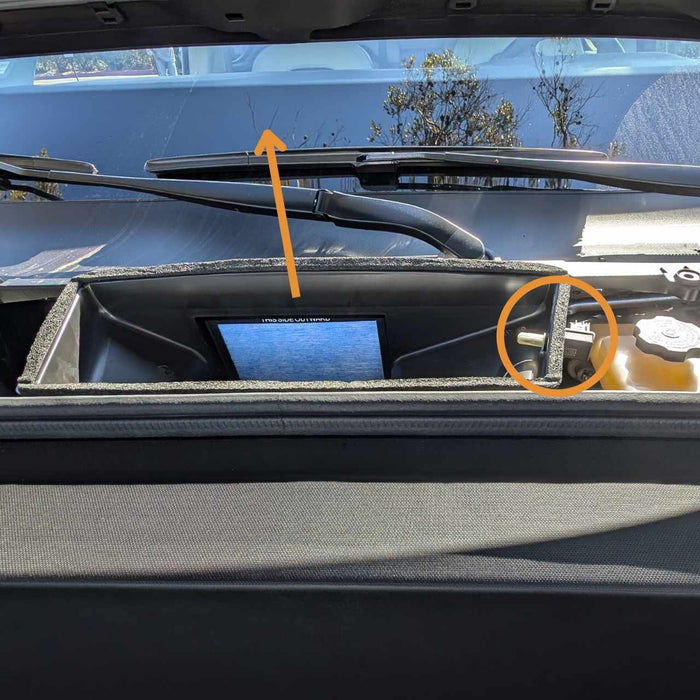 A view under a car hood showing an internal monitor and engine components with an orange arrow and circle highlighting specific parts.