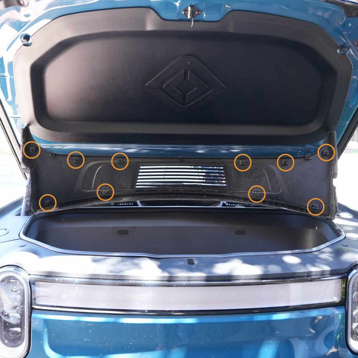Open front trunk of a blue vehicle showing storage space and air vents, with several circular markers indicating features or components.