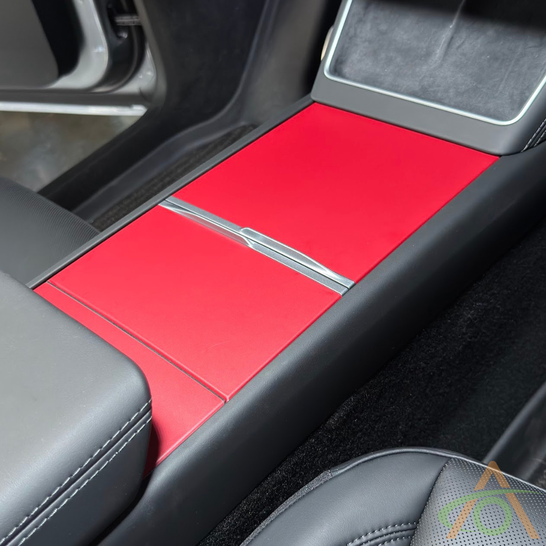 Abstract Ocean Center Console Vinyl Wrap for Refreshed Model 3 & Y shown installed, featuring a red finish with black trim accents and partially visible seat and door in the car interior.