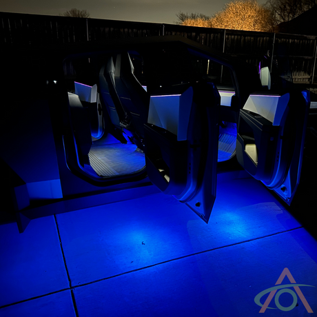Cybertruck interior illuminated by Abstract Oceans Ultrabright Lights, featuring a futuristic design with open scissor doors, glowing blue at night.