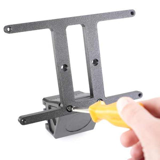 A hand uses a yellow screwdriver to tighten a screw on a black wall mount bracket.
