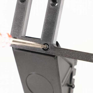 Close-up of a screwdriver tightening a bolt on a piece of black hardware with rectangular openings and a circular indentation.