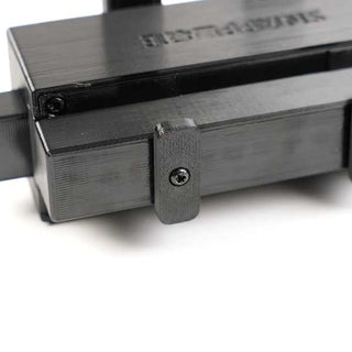 Close-up of a black mechanical component with visible screws and linear grooves, positioned on a white surface.